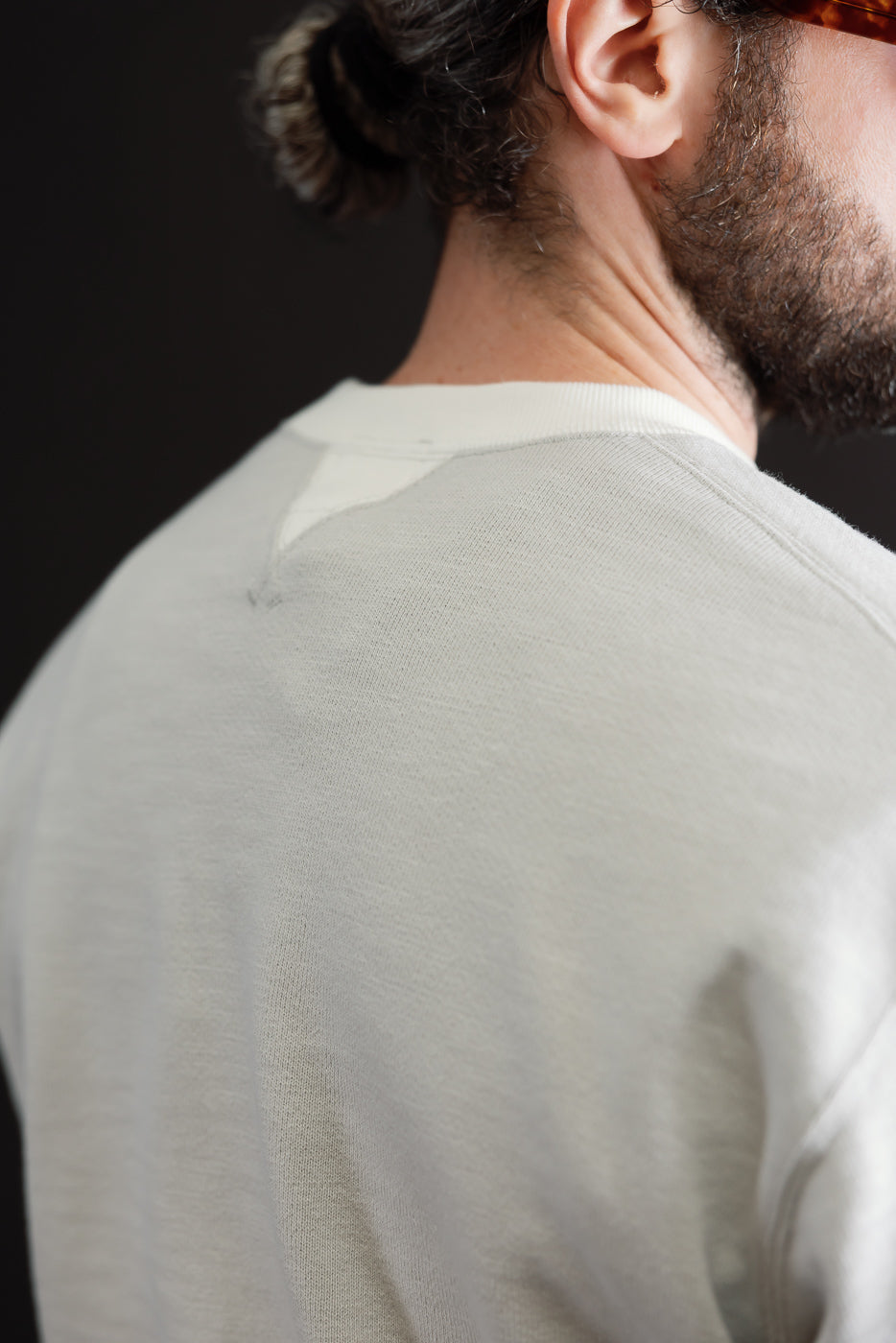 Close-up back view of a light grey sweatshirt's neckline and shoulder texture on a male model.