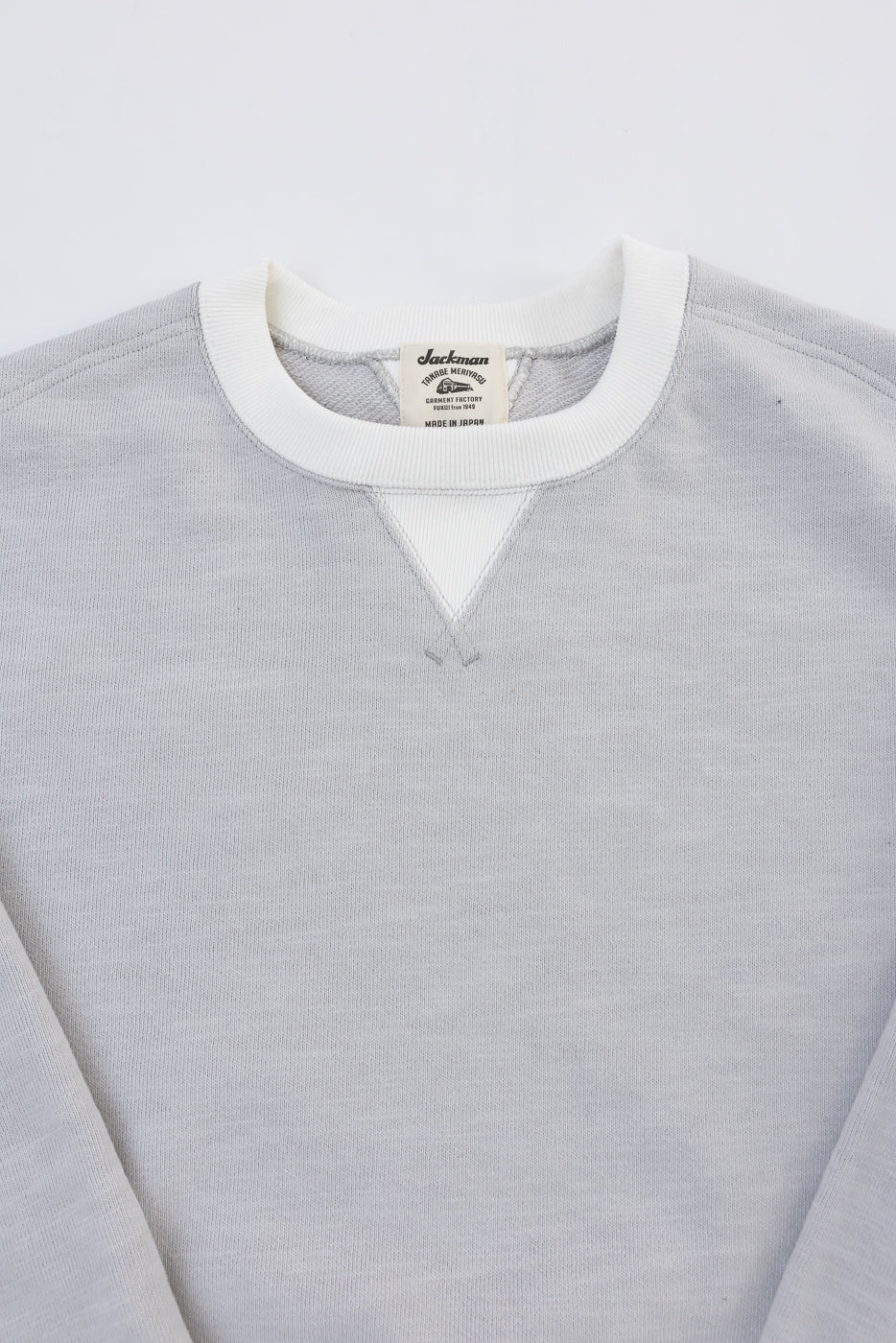 Close-up of the front neckline of a grey Jackman sweatshirt showing the white ribbed collar and brand tag.