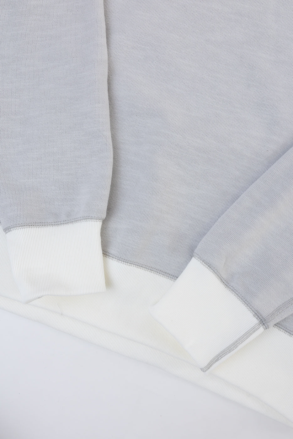Close-up of the front hem and ribbed cuffs of a light grey sweatshirt.
