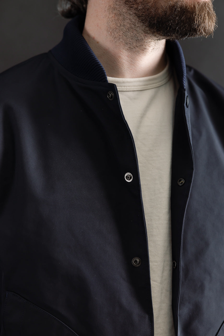 Close-up of front chest and collar on dark navy award jacket, snap buttons, ribbed collar, worn by male model 5'9