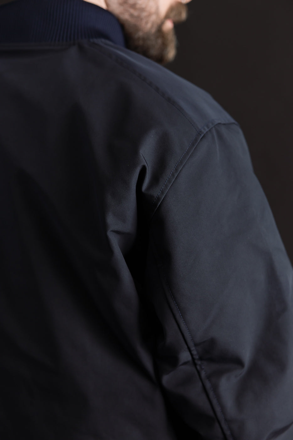 Close-up of male model's upper back and shoulder in dark navy award jacket, showing fabric texture and ribbed collar. Model is 5'9
