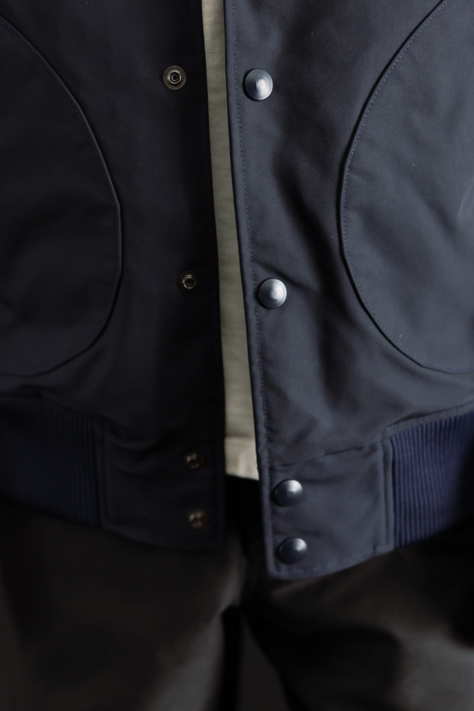 Close-up of front waist and snap buttons on dark navy award jacket, round pockets visible.