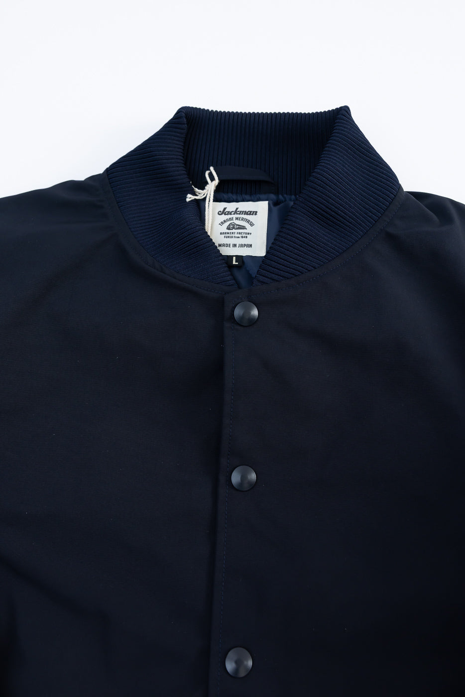 Close-up front view of navy award jacket, showing snap buttons, ribbed collar, and fabric tag detail.