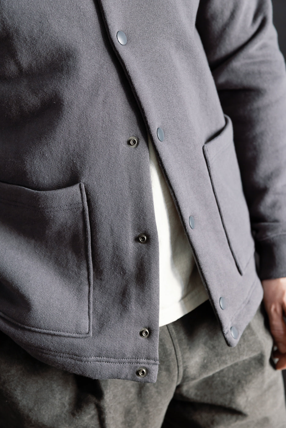 Close-up front view of men's collarless ink black snap jacket, showing pockets and buttons, on 5'9