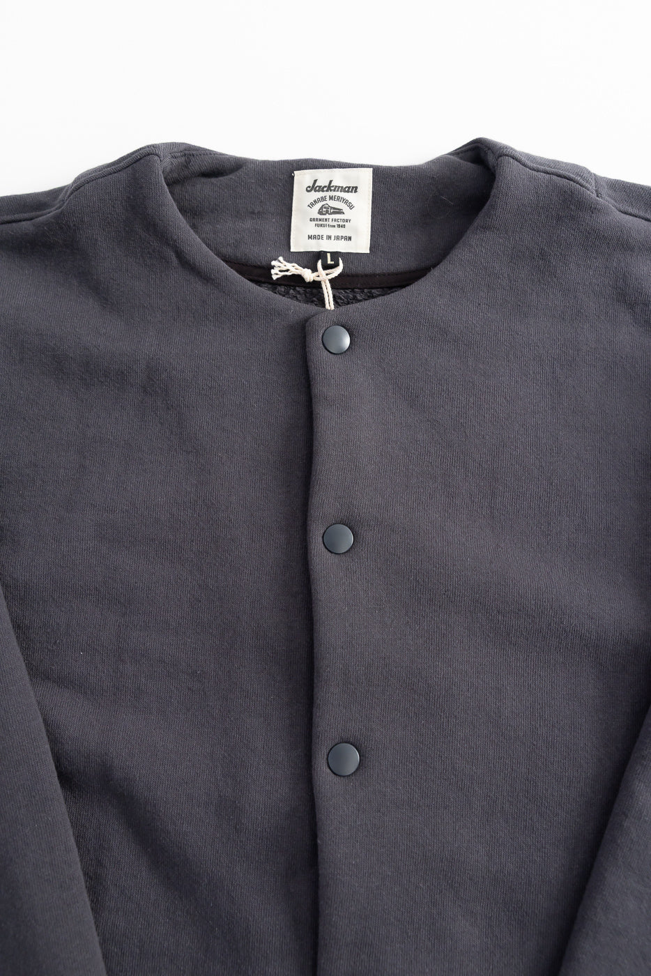 Close-up of Jackman Big Loop collarless jacket front, black snap buttons, fabric texture, front side.