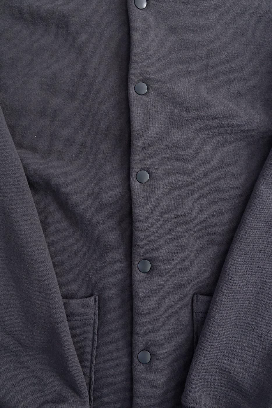 Close-up front detail of Jackman JM8580 Big Loop collarless jacket in ink black showing snap buttons, smooth knit fabric, and front pockets, contemporary casual apparel at Dant.
