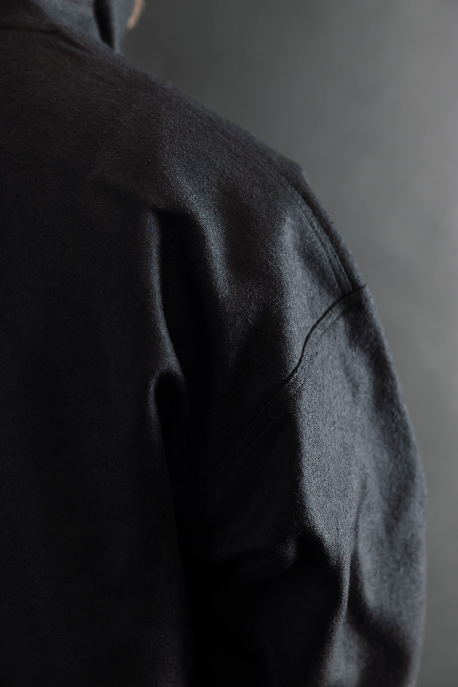 Close-up of black wool jacket back and shoulder seam, showing fabric texture and stitching.