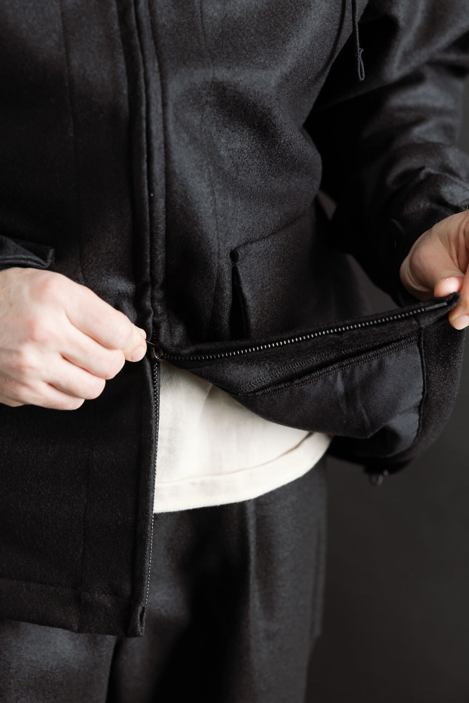 Close-up of male model, 5'9 165lbs athletic build, unzipping front of black wool jacket.