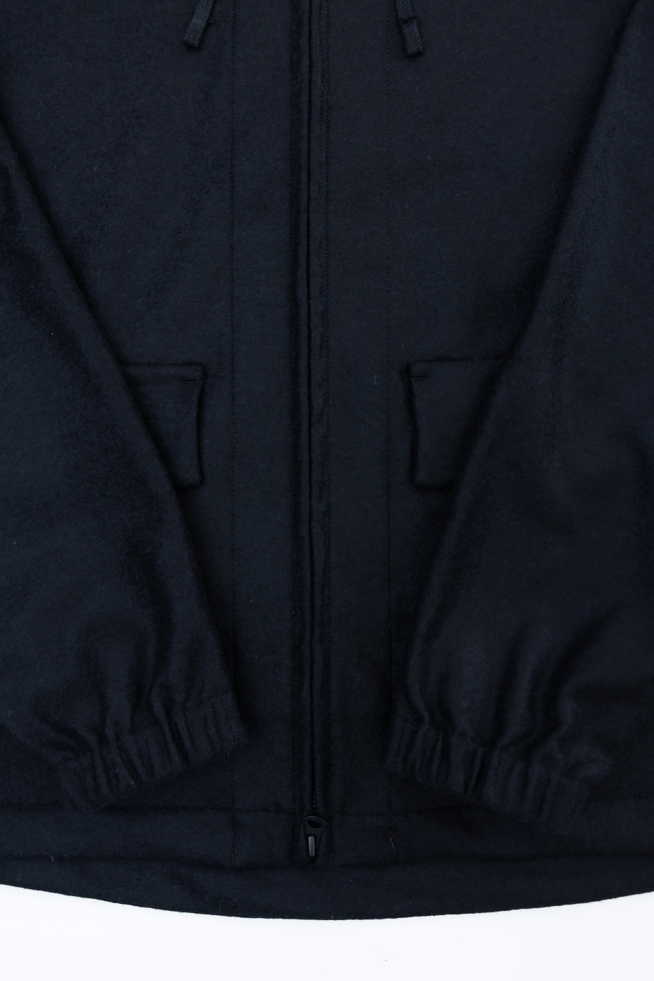 Close-up front detail of black wool jacket showing zip closure, elastic cuffs, and front pockets