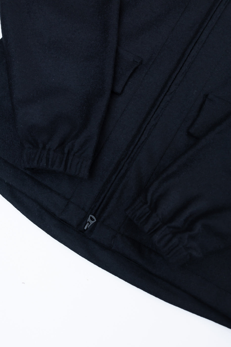 Close-up of black wool jacket front hem, zipper, lower pockets, and elastic cuffs