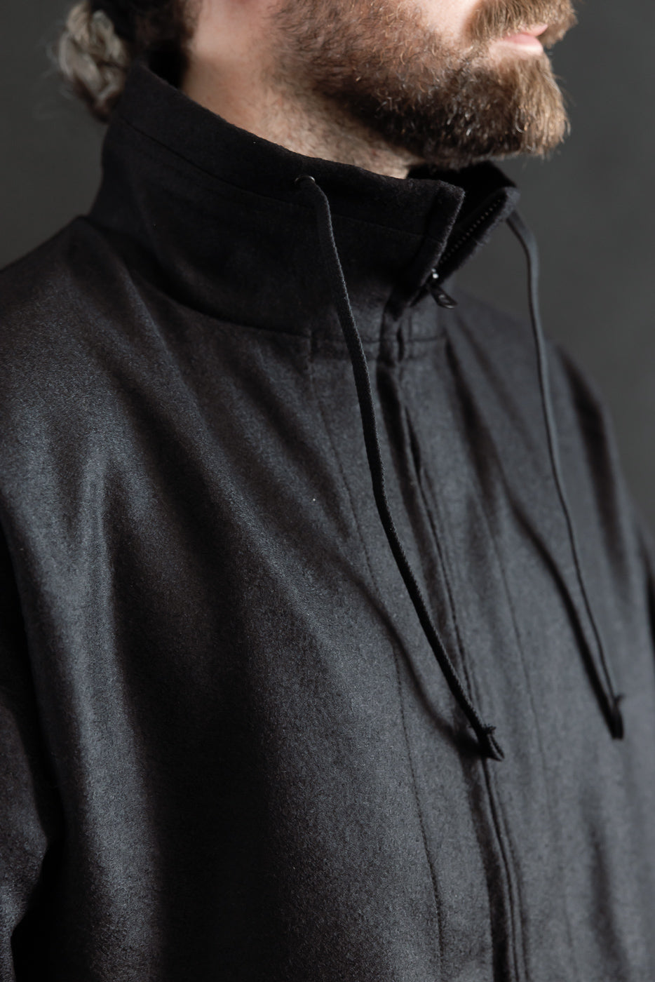 Close-up of front upper section of black wool stand neck jacket on male model, 5'9