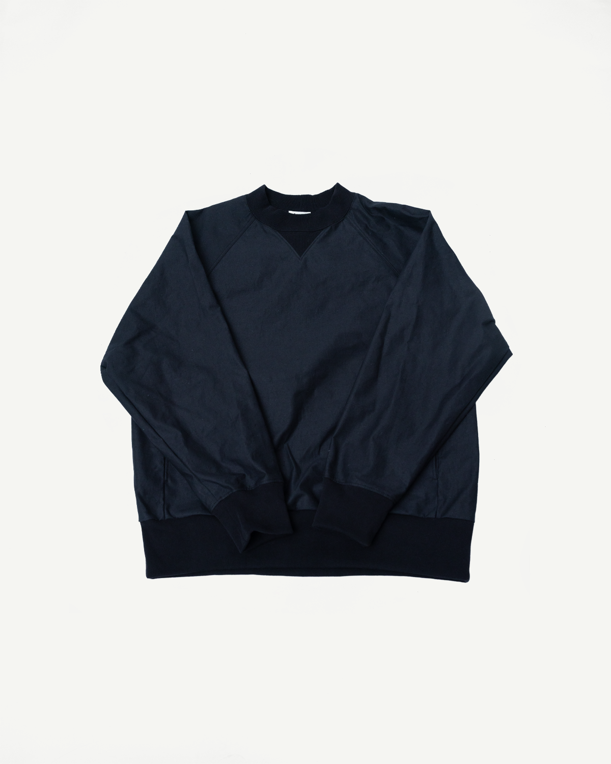 JM8615 - BN Crewneck - 07 Black: A dark navy-blue crewneck sweatshirt featuring raglan sleeves, ribbed cuffs, a triangular stitch below the collar, and seam pockets, showcasing a textured, rustic surface.