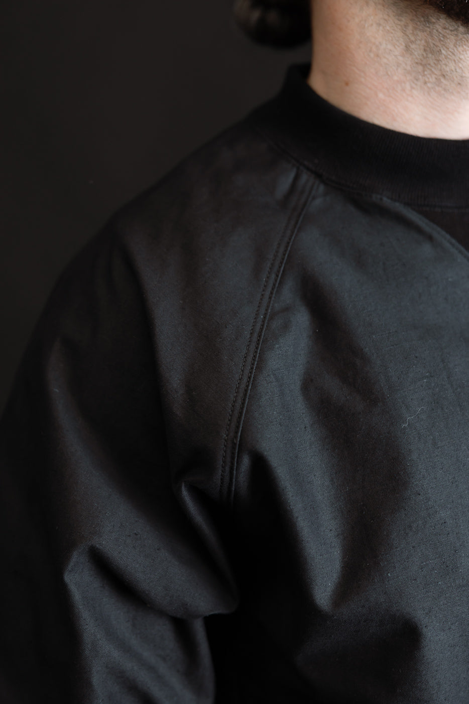 Close-up of the JM8615 - BN Crewneck - 07 Black, showcasing its textured nep yarn fabric and precise stitching on the shoulder and chest, with a ribbed crewneck collar highlighting its craftsmanship.