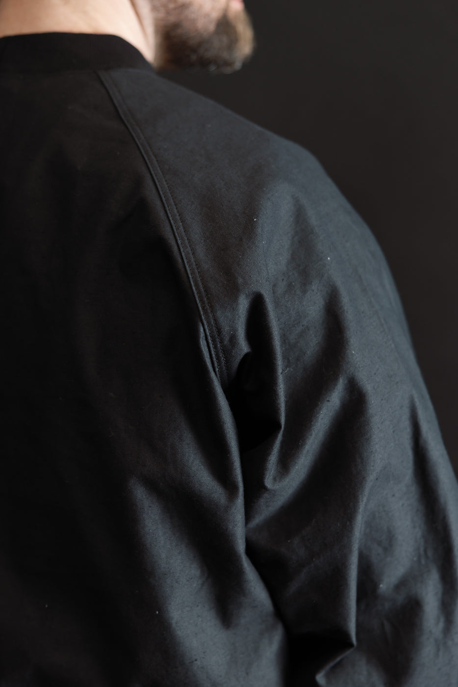 Close-up of a person wearing the JM8615 - BN Crewneck - 07 Black, highlighting the textured nep yarn fabric and classic raglan sleeve design, emphasizing the garment's voluminous, loose fit.