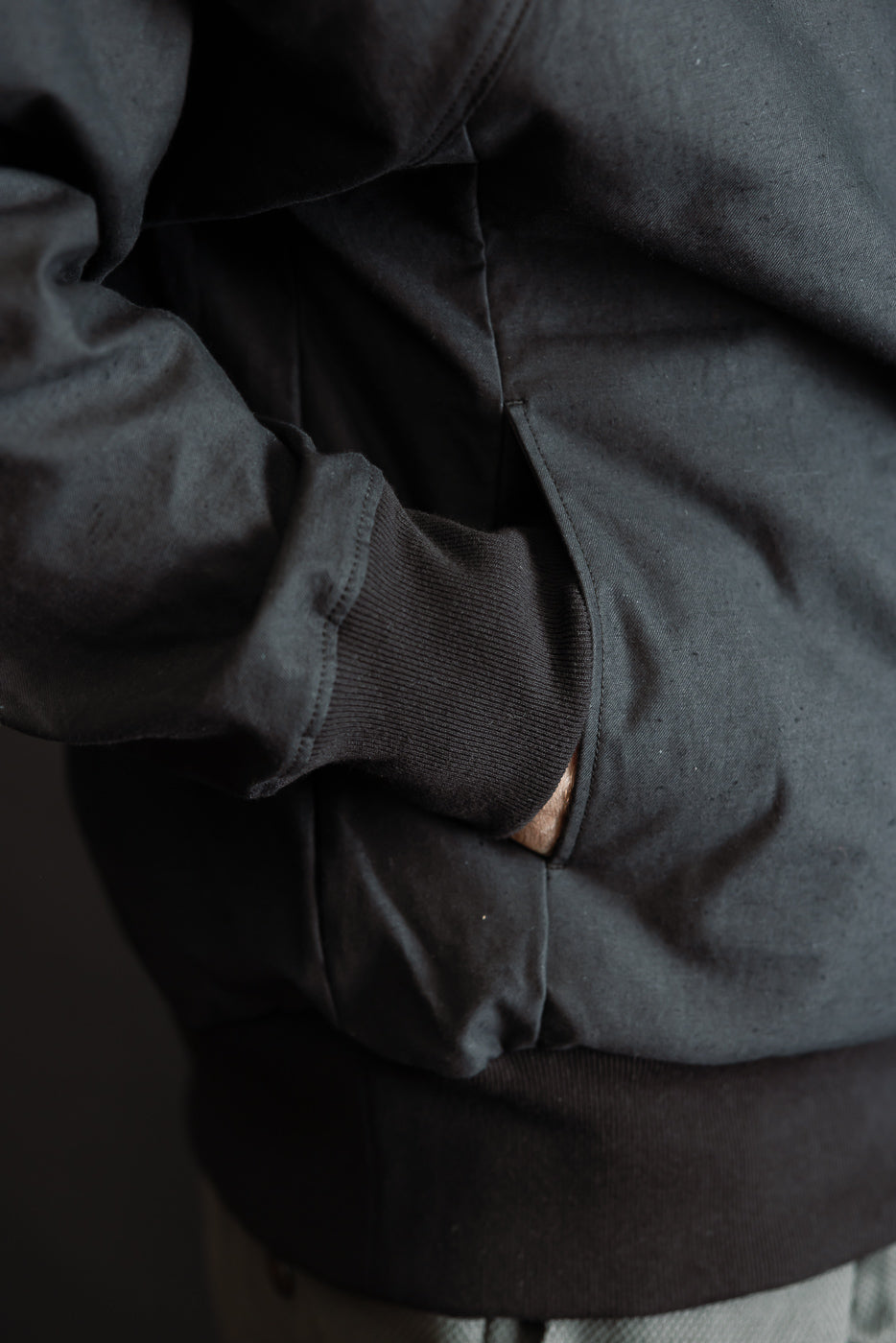 Close-up of JM8615 - BN Crewneck - 07 Black, showcasing the ribbed cuff, waistband, and hand in kangaroo pocket, highlighting the garment's textured nep yarn fabric and voluminous, loose fit.