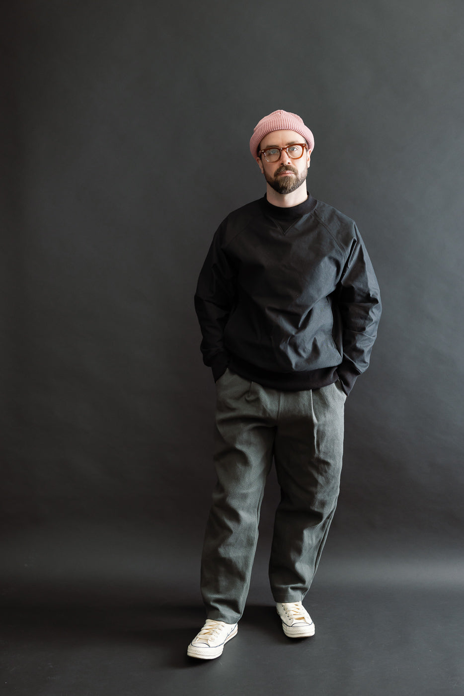 Man wearing JM8615 - BN Crewneck in black, featuring a voluminous fit with raglan sleeves and mid-neck V-gusset. Styled with gray trousers and white sneakers, embodying Dant's premium heritage-inspired fashion.