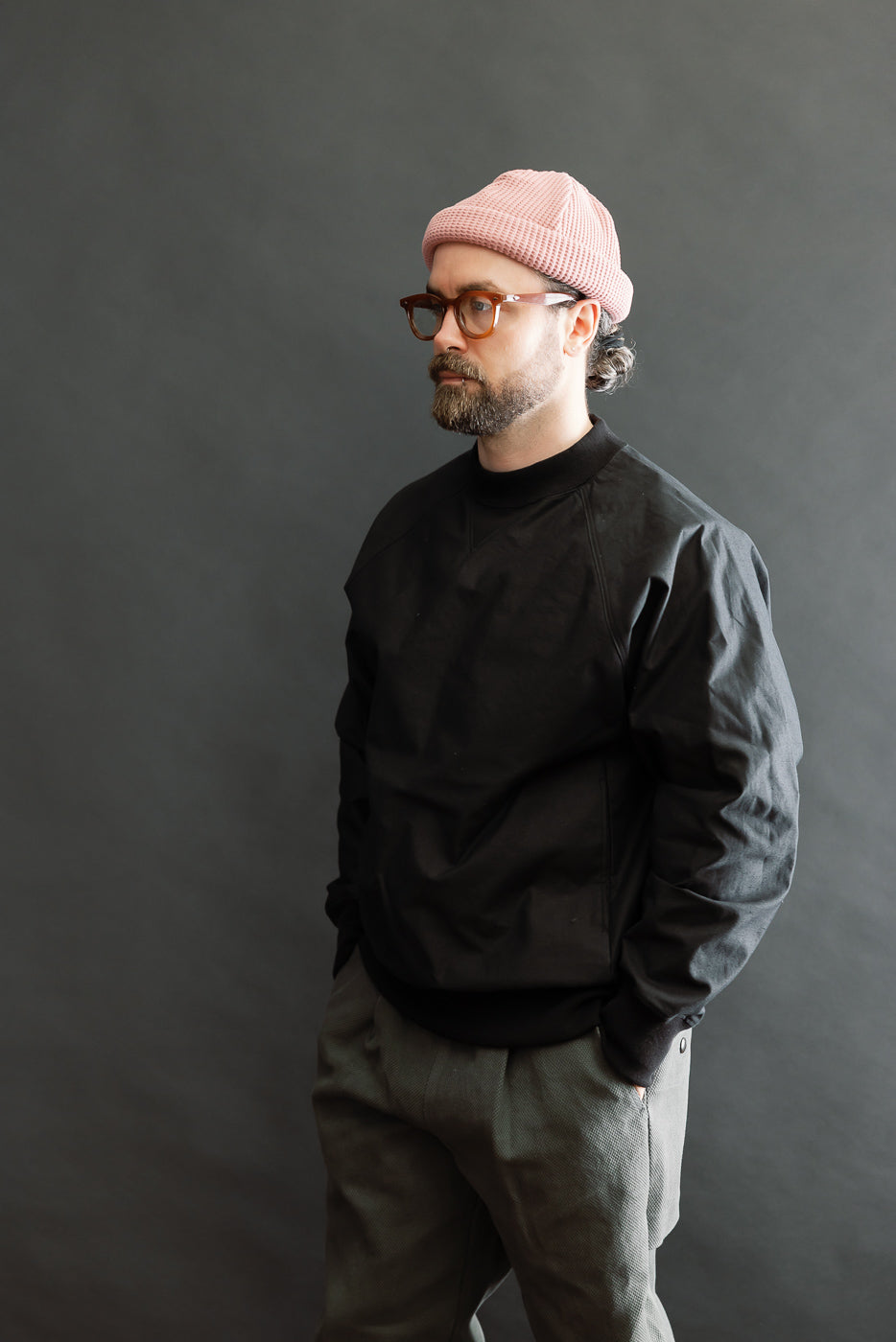 A bearded man in a JM8615 - BN Crewneck - 07 Black displays the pullover's loose fit and raglan sleeves, highlighting its rustic, nep-yarn texture.
