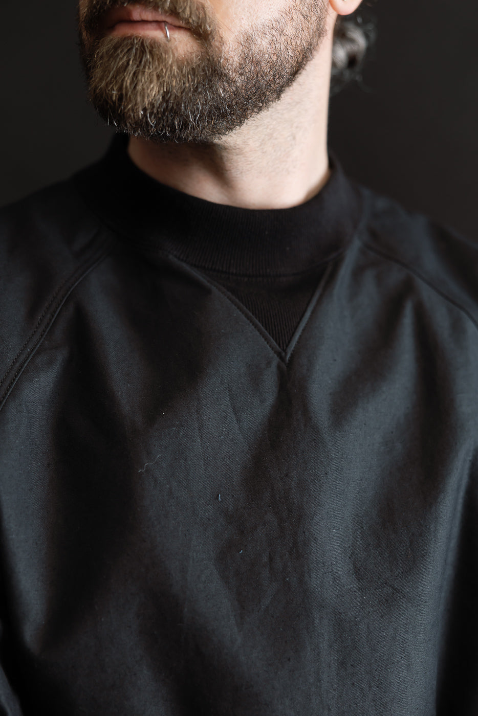 JM8615 - BN Crewneck - 07 Black showcased on a model's torso, highlighting its mid-neck with V-gusset and classic raglan lines, crafted from nep yarn for a textured, rustic finish.