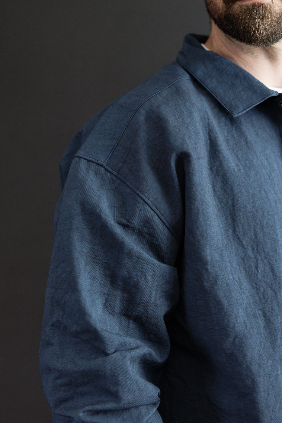 Close-up side view of male model in navy linen shirt, showing collar, shoulder seam, and textured fabric detail