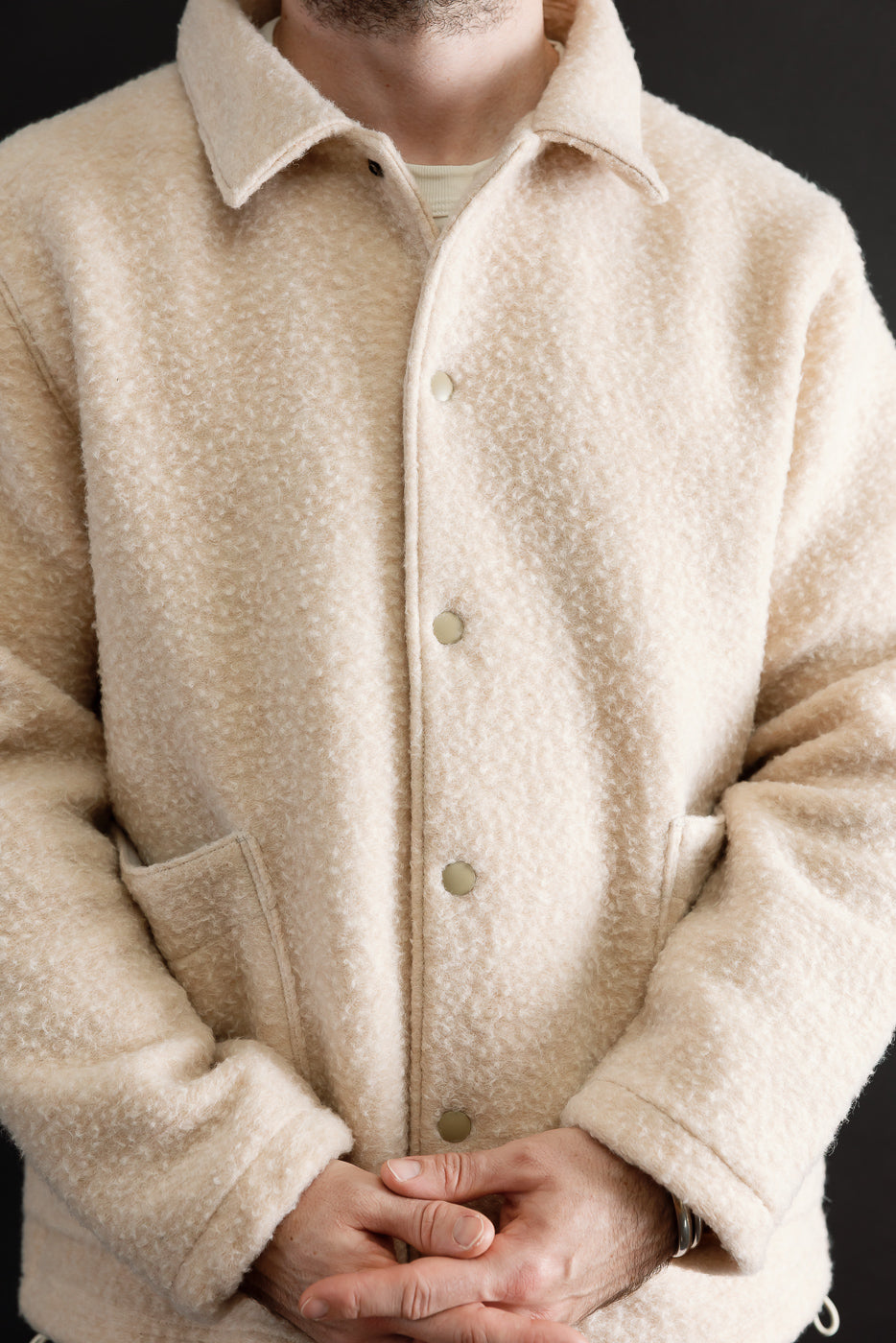 Front view close-up of a male model wearing a cream textured fleece jacket with button closure.