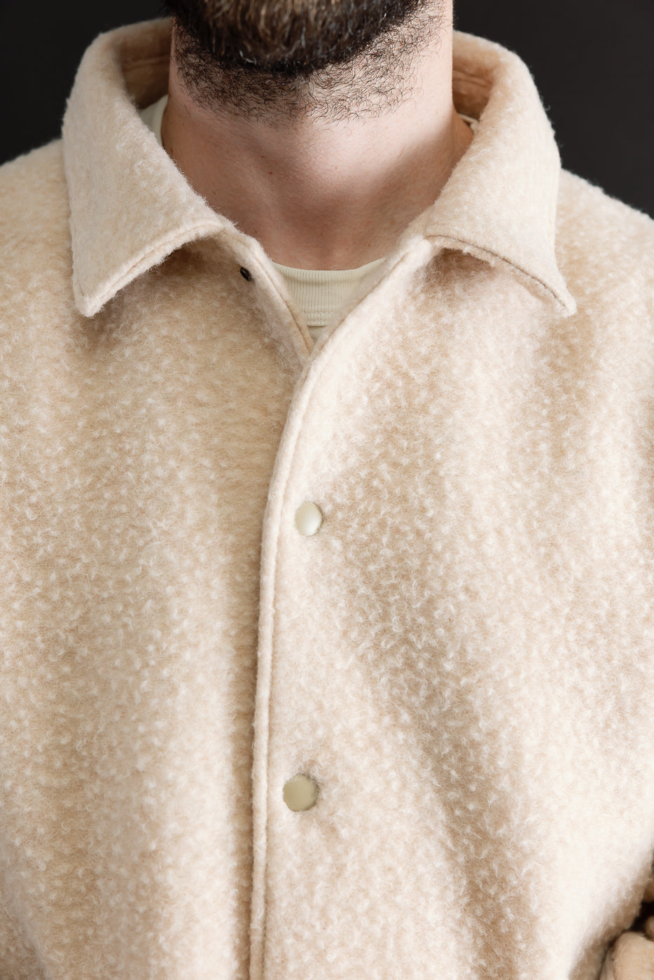 Close-up front view of a cream textured wool jacket showing the collar and button details.