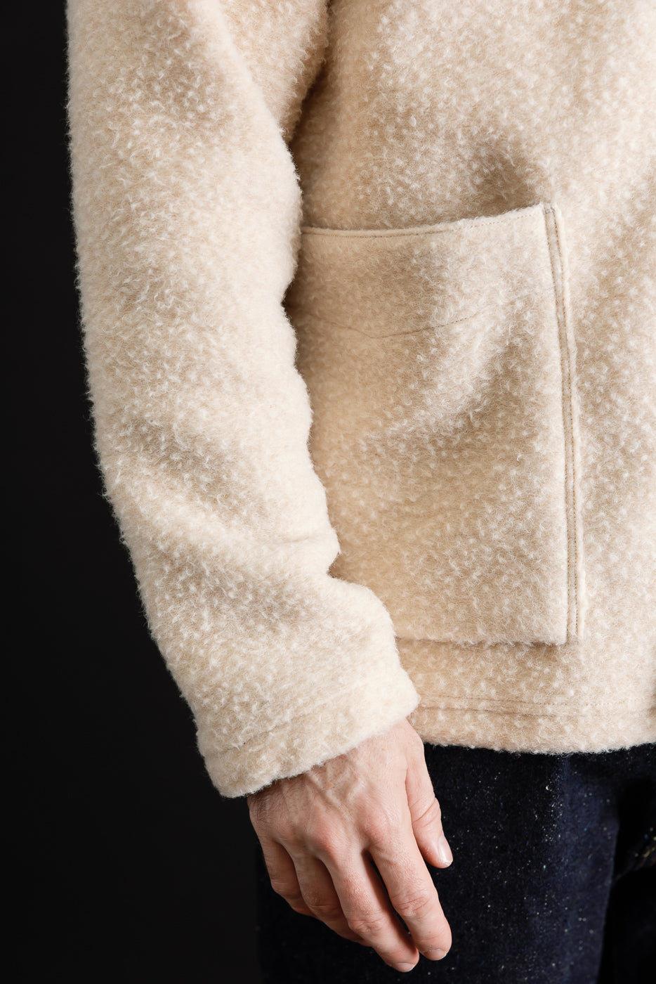 Close-up of the front texture and pocket of a cream-colored sherpa fleece jacket worn by a male model.