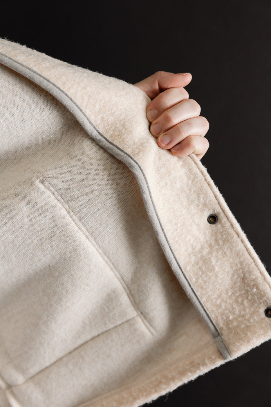 Close-up of the front texture and grey piping detail on a cream fleece jacket.