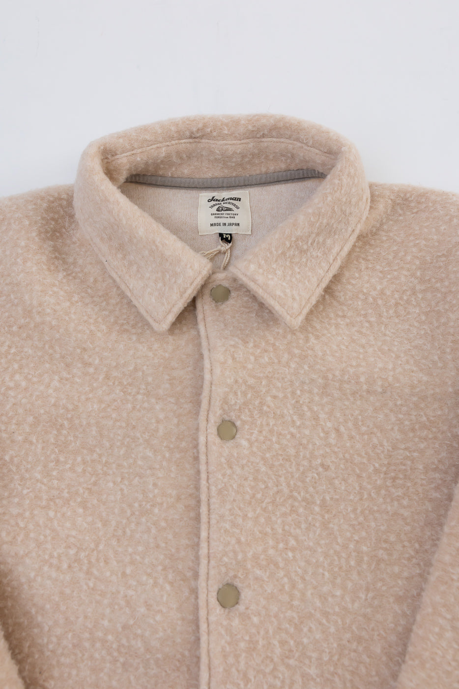 Close-up of the front collar and neckline of a beige textured fleece jacket showing the tag.