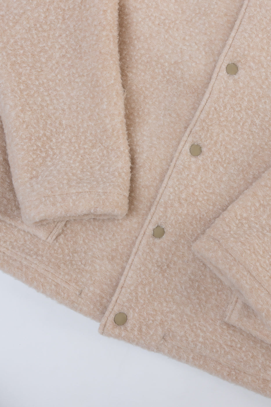 Close-up of the front right side of a beige fuzzy fleece jacket showing gold snap buttons.