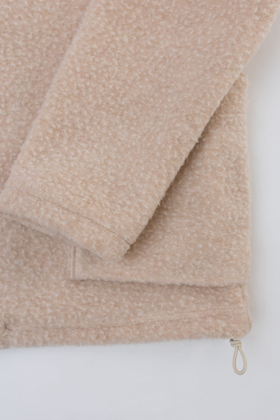 Close-up of the bottom hem and drawstring detail on a beige fleece garment, front view.