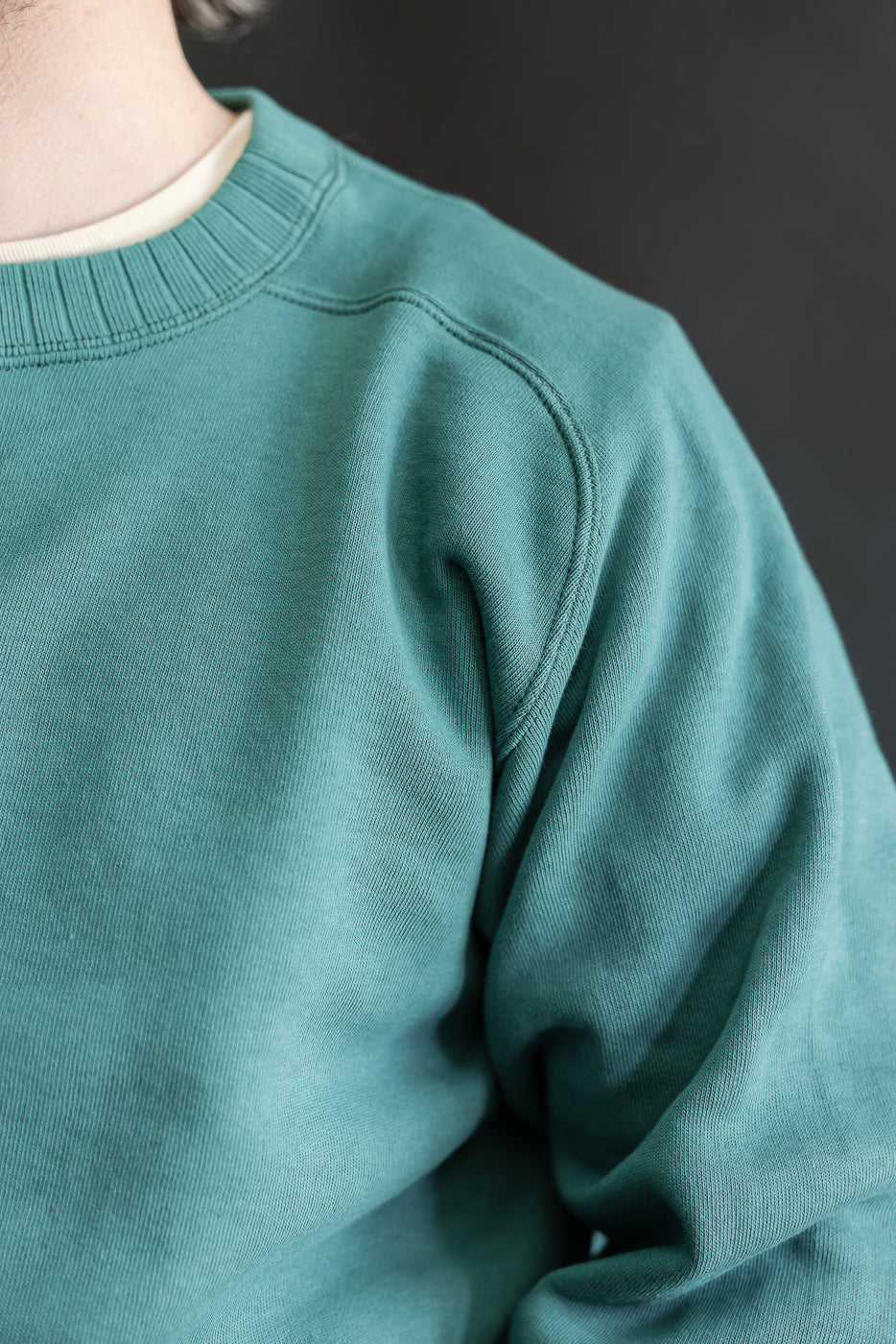 Model wears the JG-CS24 - The Albert Sweat - Blue Green, showcasing its crew-neck design and freedom sleeve construction, highlighting the garment's soft texture and seamless, relaxed fit.