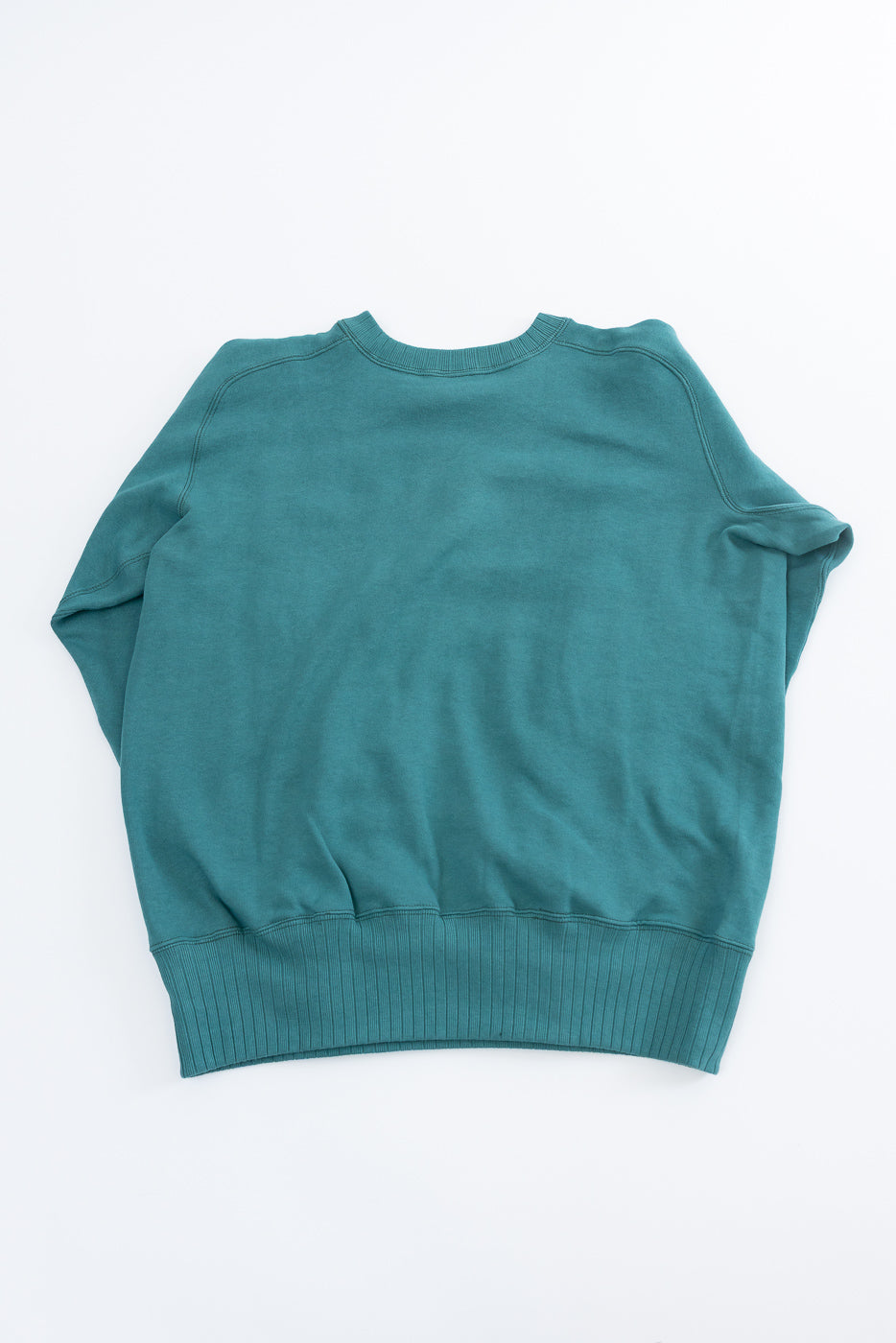 JG-CS24 - The Albert Sweat - Blue Green: Back view of a teal-blue crewneck sweatshirt with seamless sides and freedom sleeves, inspired by 1940s sportswear, laid flat on a white background.