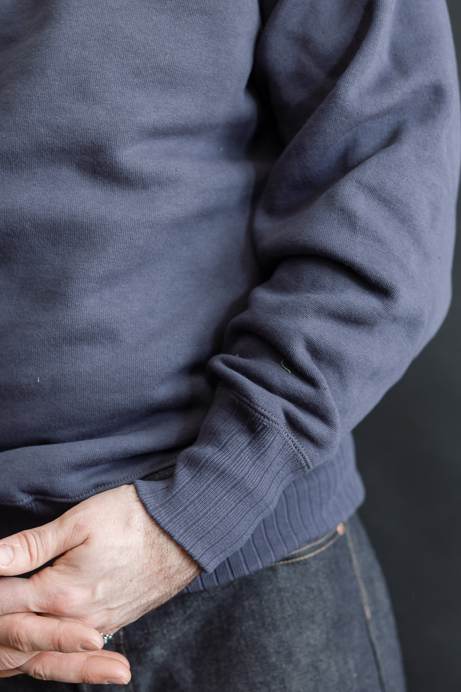 JG-CS24 - The Albert Sweat - Eggplant: Person wearing a navy long-sleeve sweatshirt with a relaxed fit, showcasing a classic silhouette and freedom sleeve construction, complemented by dark jeans and a visible keyring.