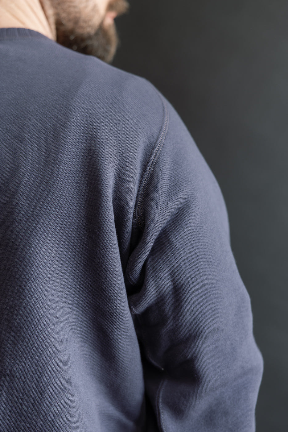 Close-up of the JG-CS24 - The Albert Sweat showcasing its navy-blue knit fabric, highlighting the intricate stitching and unique freedom sleeve design, reflecting vintage sportswear style.