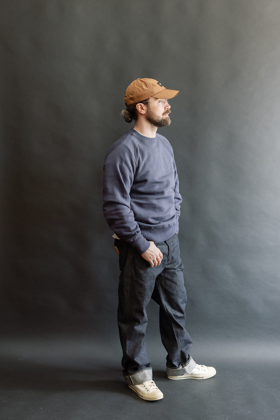 The John Gluckow JG-CS24 Albert Sweat in Eggplant is worn by a model in a studio, highlighting its classic crewneck design and relaxed fit.