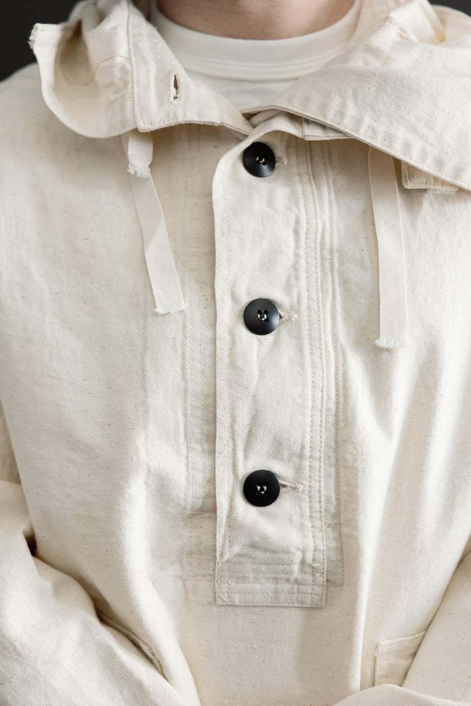 Close-up front view of off-white sailor pullover parka on male model, highlighting button placket, drawstring hood, and fabric texture.