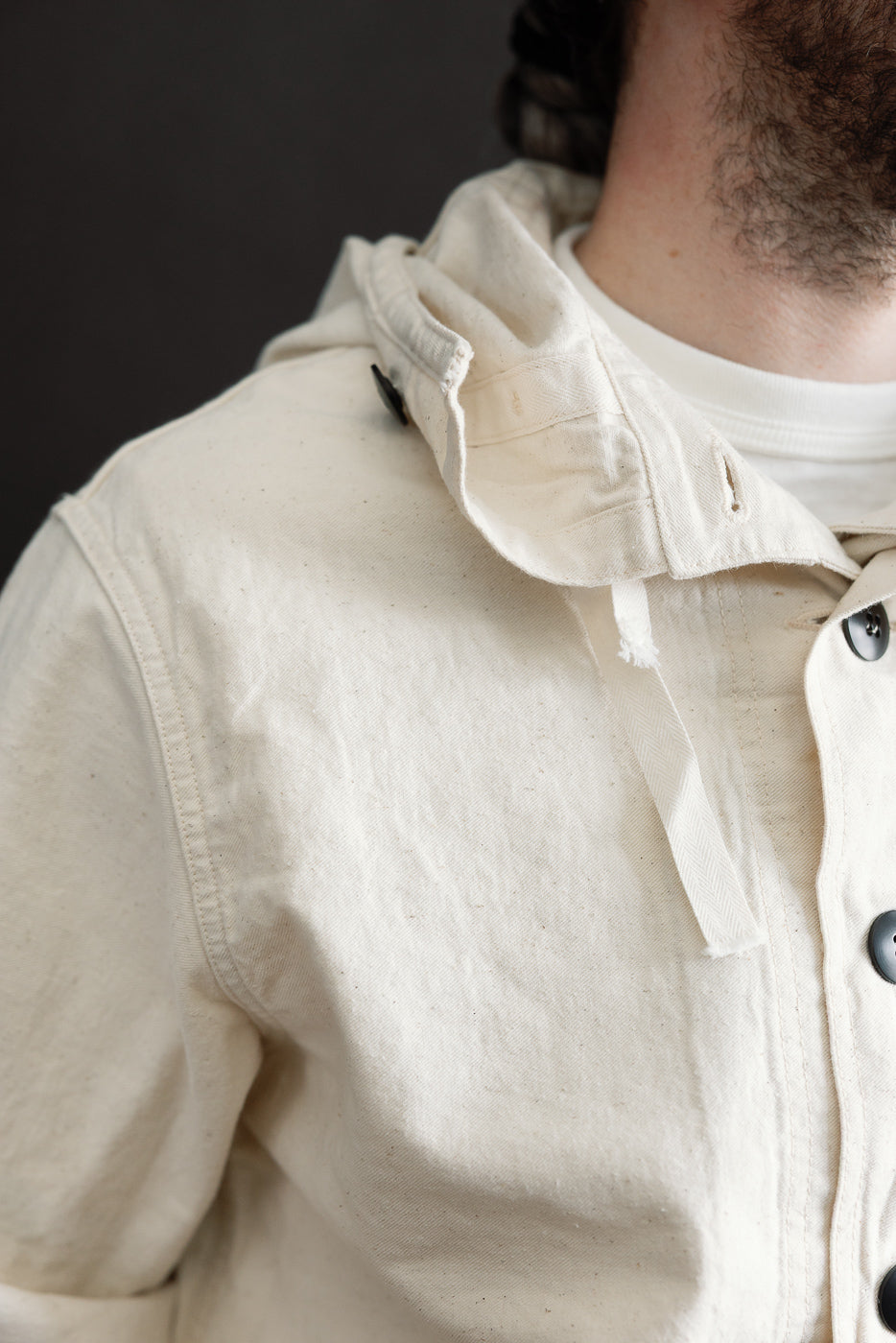 Close-up of front chest and hood area on off-white sailor's parka, male model 5'9 165lbs athletic build, showing fabric texture, buttons, and collar detail.
