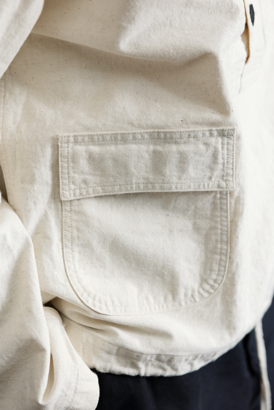 Close-up of front left pocket on off-white pullover parka, showing flap and fabric texture.