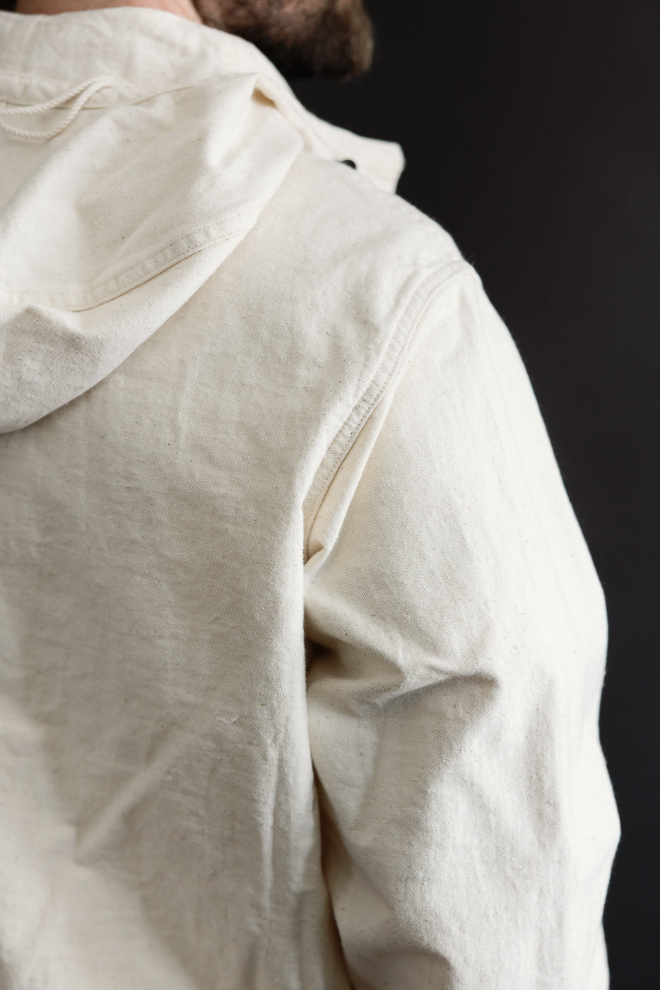 Close-up of the back and shoulder of off-white sailor pullover parka, showing fabric texture on male model, 5'9