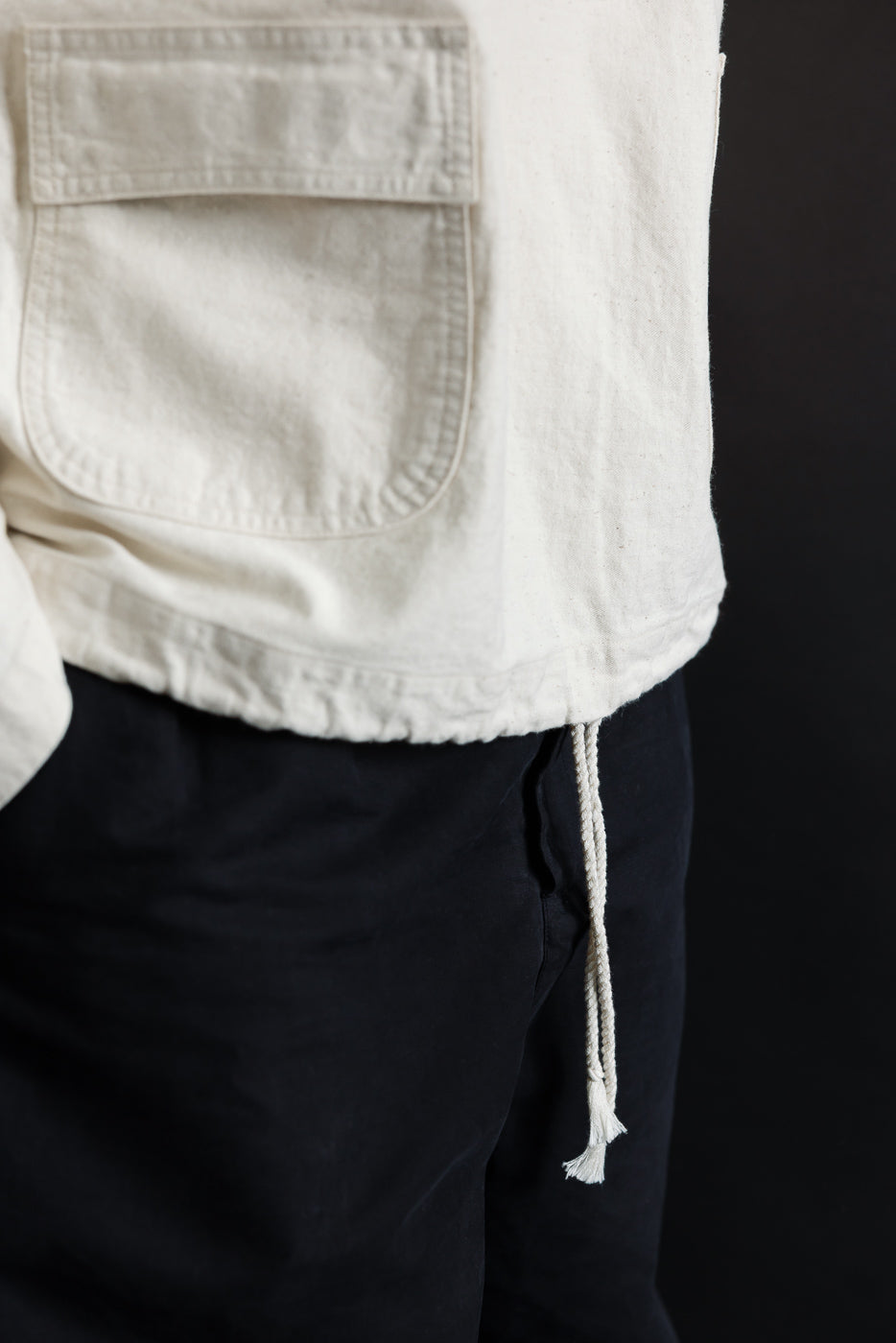Close-up of off-white sailor pullover parka front hem, pocket flap and drawstring, on male model, 5'9