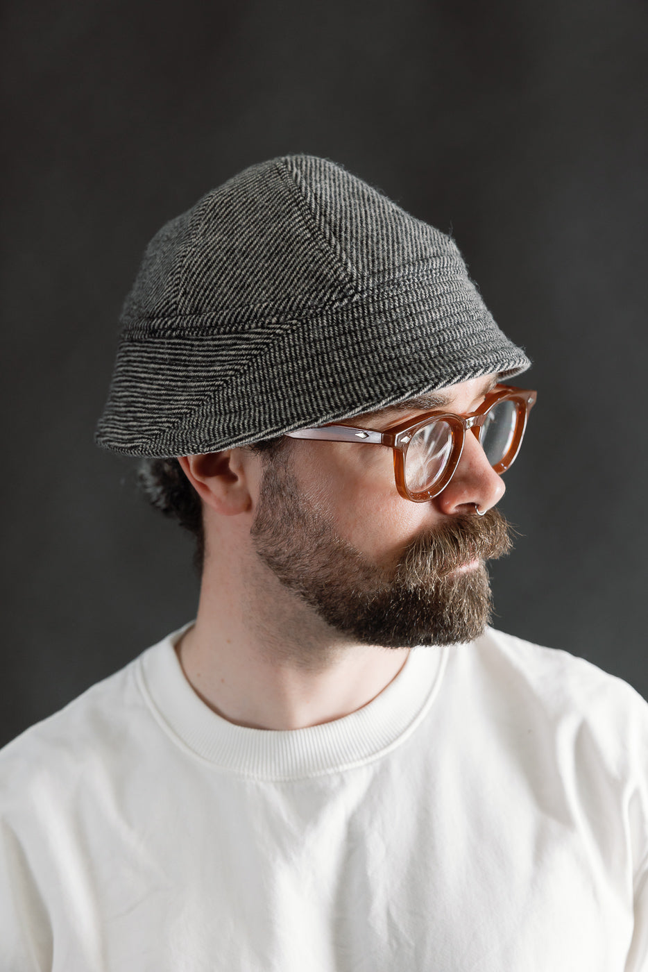 Male model 5'9, 165lbs, athletic build in close-up right side view, wearing John Gluckow Lot JG-31 Tweedy Prison Cap in beige herringbone fabric, visible texture and panel seams, casual contemporary style, Dant apparel.
