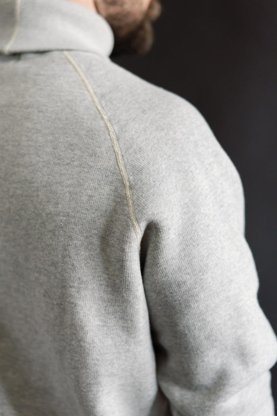 Close-up of male model's athletic upper back and shoulder in Loop & Weft vintage grey raglan turtleneck, showing fabric texture and stitching detail.
