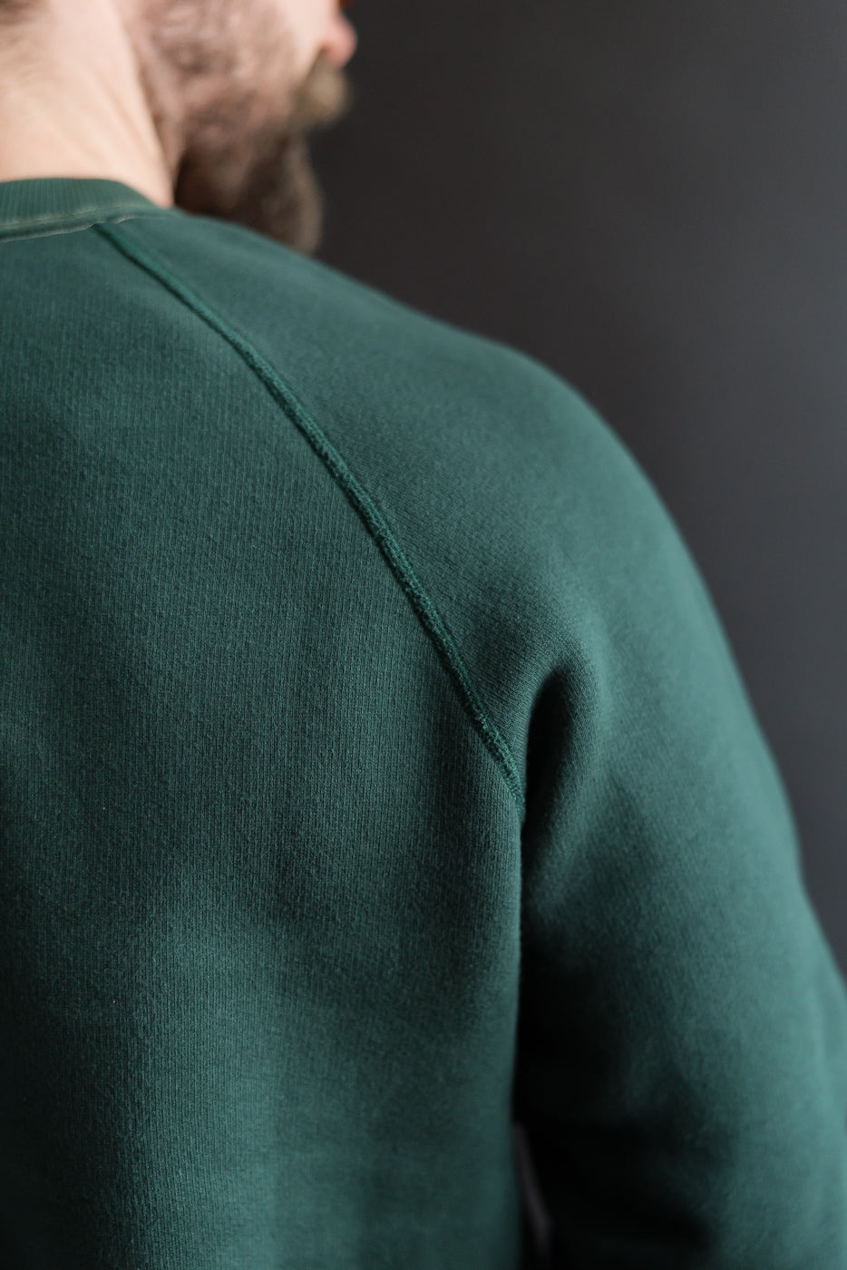 Close-up of male model's left shoulder wearing Loop & Weft Super Fluffy Knit raglan crewneck in vintage forest green, showcasing fabric texture and seam detail.