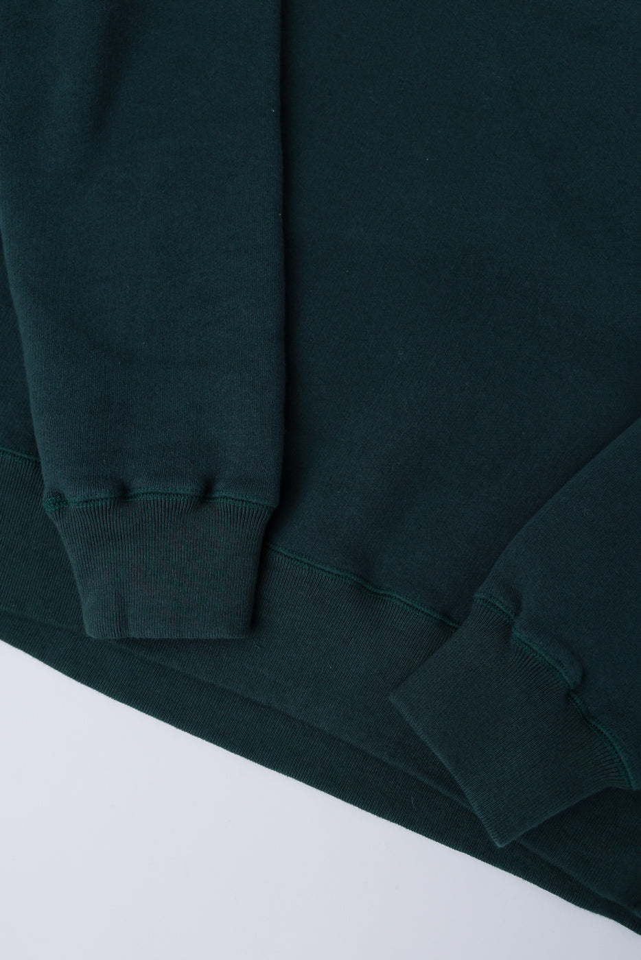Close-up of Loop & Weft forest green crewneck sweatshirt sleeves and hem, front view.