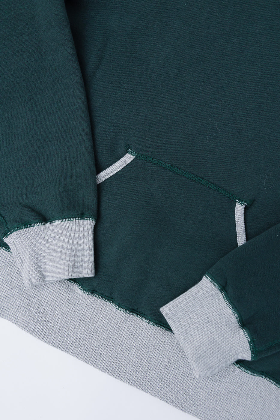 Close-up of forest green and grey knit hoodie front pocket, cuffs, and hem detail, flat lay