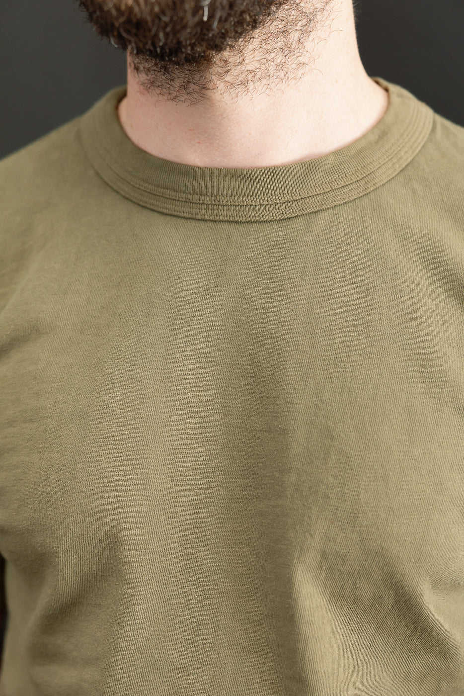 Close-up front view of olive green t-shirt on male model, showcasing ribbed crew neck and fabric texture