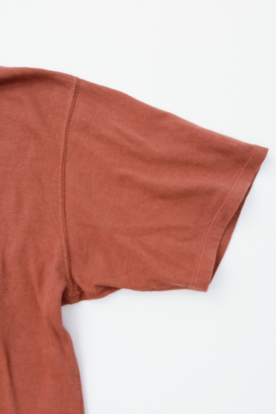 Close-up of rust-colored t-shirt sleeve, showcasing fabric texture and hem detail
