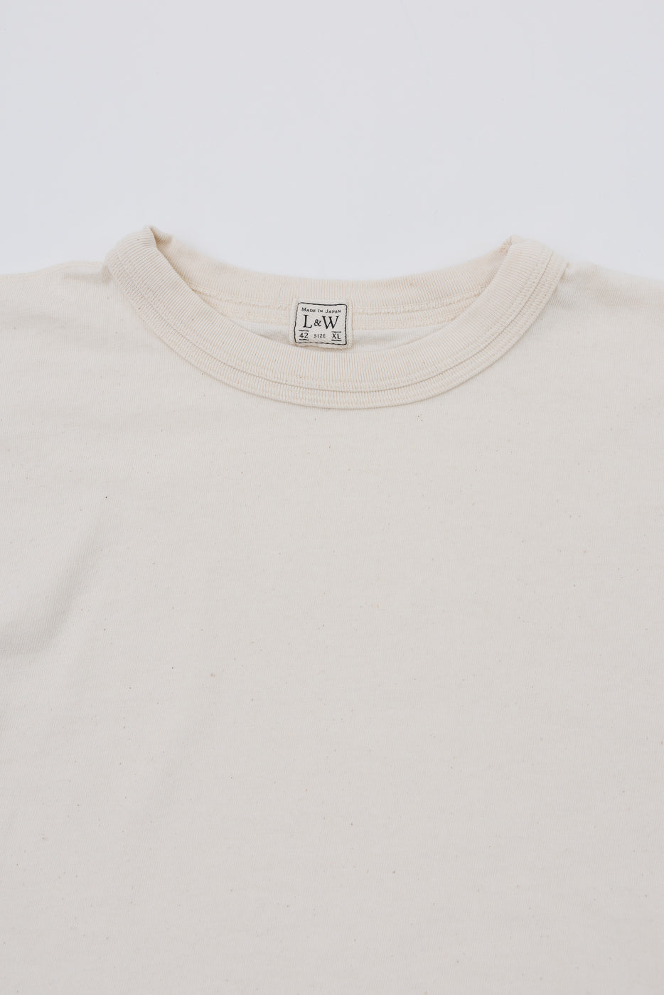 Close-up of cream t-shirt collar with L&W tag, front view, showing fabric texture and label details