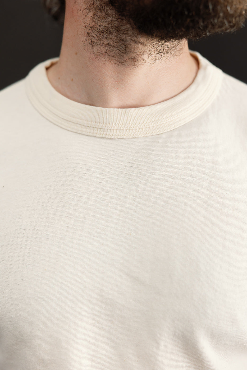 Close-up front view of cream crew neck tee on male model, showing ribbed collar detail and soft fabric texture
