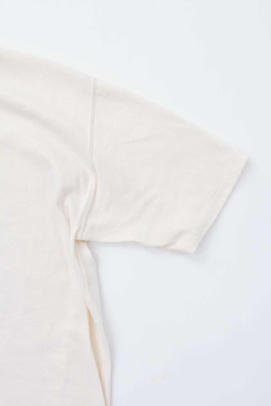 Close-up front view of off-white t-shirt sleeve, showing side seam and ribbed hem detail, soft cotton texture